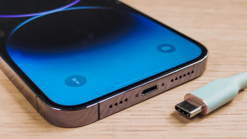 Close-up da porta USB-C de um iPhone moderno ao lado de um cabo USB-C, sobre uma superfície de madeira.