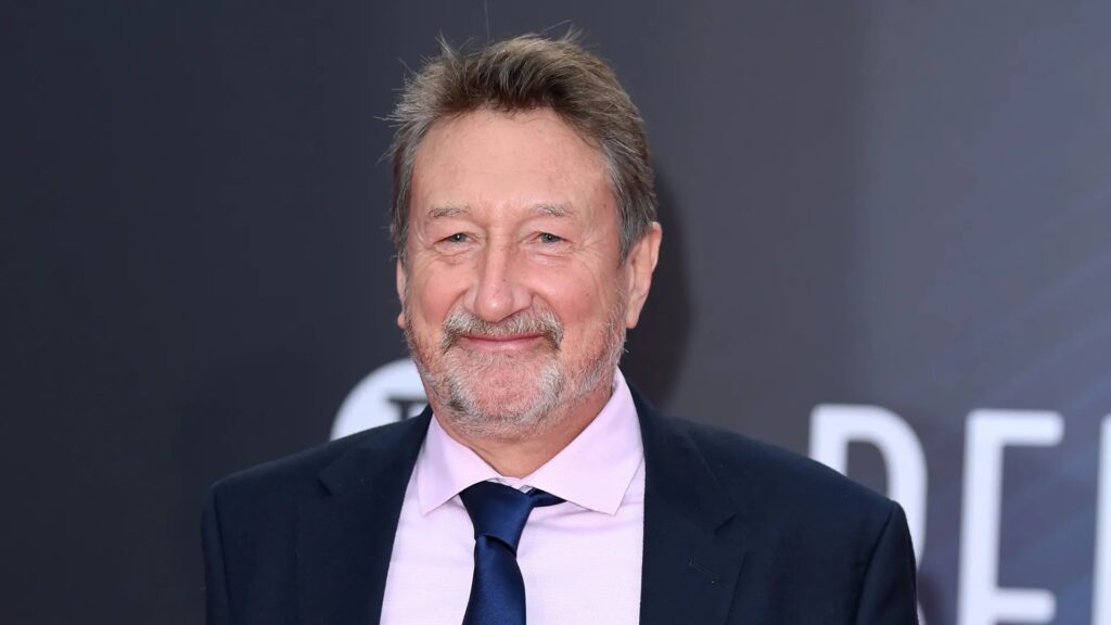 Close-up do roteirista Steven Knight sorrindo em um evento de tapete vermelho.