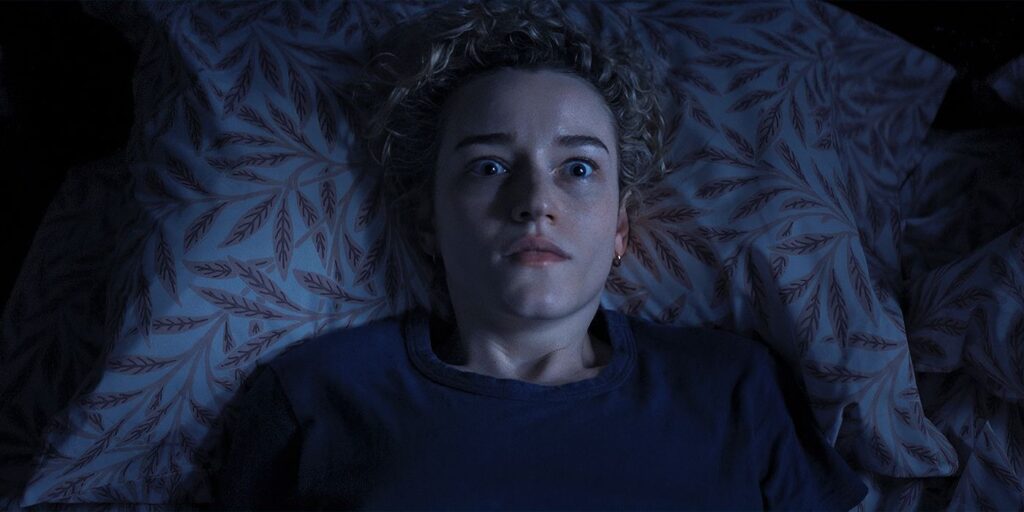 Julia Garner como a professora Justine Gandy deitada na cama com uma expressão de terror no filme 'A Hora do Mal' (Weapons).